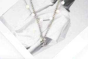 Detail of a layered men's titanium steel chain with white pearls and a Paris engraved pendant
