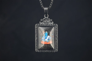 Detailed close-up of a Tibetan Thangka Medicine Buddha pendant with engraved silver frame