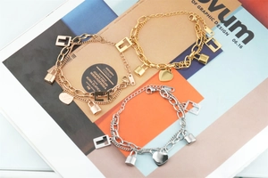 Detail of double-layer chain bracelets with heart and lock charms in gold and silver