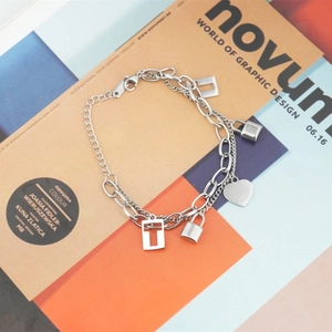 Double-layered silver titanium steel bracelet with heart and lock charms on art magazine