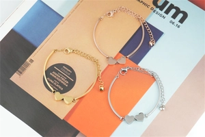 Three minimalist heart pendant bracelets in gold, silver, and rose gold on a design magazine