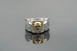 Macro detail of punk skull ring featuring golden shield with silver wings and texture