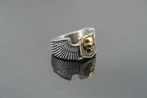 Detail of a punk skull ring with silver wings and golden accent on a reflective surface