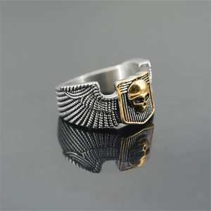 Punk style stainless steel skull ring with silver wings and gold skull on dark mirror surface