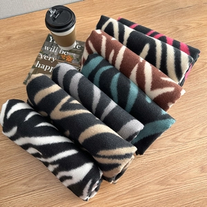 Multiple zebra print knit scarves in various colors on a wooden desk with a coffee cup
