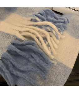 Close-up of blue and white plaid scarf featuring thick knit fabric and fluffy tassels