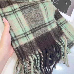 Close-up of mint green and brown plaid knit scarf showing soft brushed texture and tassels