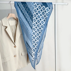 Elegant blue geometric pattern silk scarf displayed on a white hanger with a beige blazer