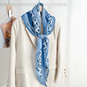 Elegant blue silk scarf with geometric patterns draped on a beige blazer for stylish look