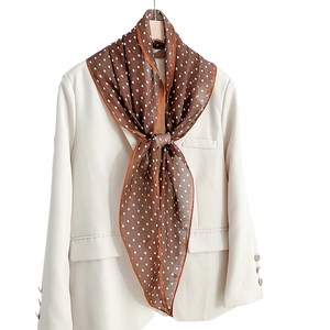 Brown polka dot silk scarf draped over a cream blazer with elegant vintage styling