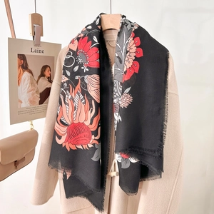 Black winter scarf with large red floral print and fringe details worn over a beige coat