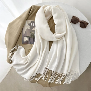 Elegant cream cashmere-feel scarf with fringe, laid on suit with stylish magazines