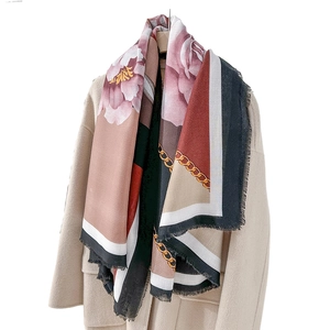 Elegant floral silk scarf with geometric border and fringe edge on a beige coat