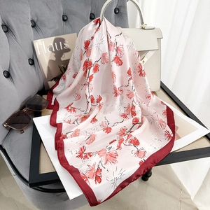Elegant floral print silk scarf in pink and red draped over a luxury handbag