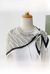 Detail view of a black and white striped triangle scarf on a white shirt and pearl necklace