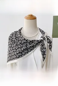 Detailed view of a black paisley silk neck scarf on a model with pearl necklace