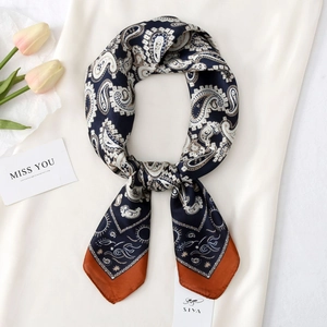 Detailed view of dark navy paisley silk scarf with orange borders on satin background