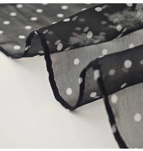 Close-up of lightweight black mesh fabric with white polka dots and delicate edge stitching
