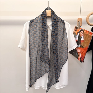 Detail of silk scarf featuring silver leaf patterns on navy blue hung on wood hanger