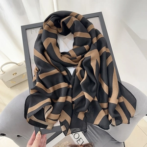 Long linen scarf with black and brown geometric stripes on a gray fabric chair