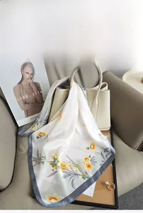 Close-up of silk-like floral scarf with yellow flowers tied on a beige leather handbag