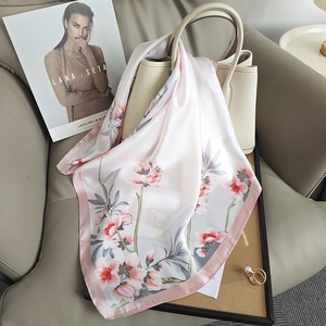 Elegant silk scarf with pink floral patterns draped over a beige leather luxury handbag