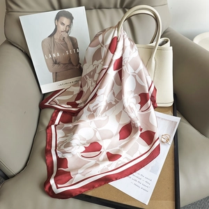 Carré de soie aux motifs floraux bordeaux élégamment noué sur un sac à main blanc