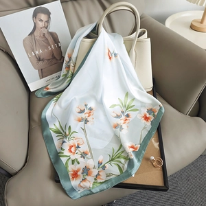 Elegant silk scarf with floral pattern and green border draped on a luxury handbag