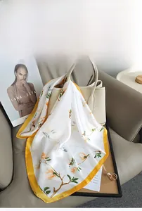 Détail d'un foulard carré en soie à fleurs sur un sac à main beige élégant