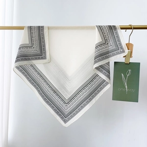 Detail view of a beige paisley silk cotton square scarf hung on a golden metal rod