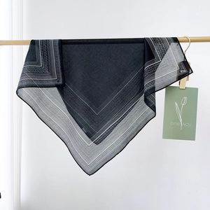 Vintage black silk square scarf with white paisley pattern hung on a metal rack