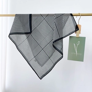 Elegant black and white striped silk scarf hanging on a gold rod with a minimalist card