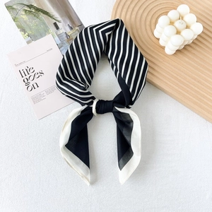 Close-up of black and white striped silk scarf tied in a bow on a wooden tray