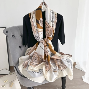 Detail of elegant satin scarf with floral camellia print draped on a grey velvet chair