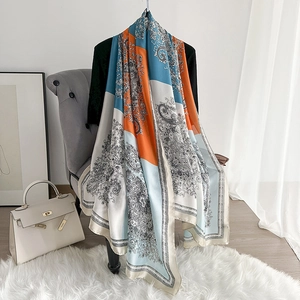 Detail of thin silk scarf with blue paisley patterns draped over a grey sofa