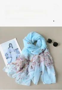 Detail of light blue floral scarf made of lightweight yarn styled with sunglasses