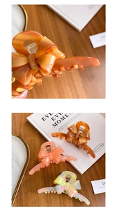 Detail shot of large acetate bow hair claws in marble and coral on a wooden table