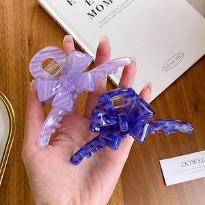 Handheld display of large acetate bow hair claws in purple and blue marble patterns