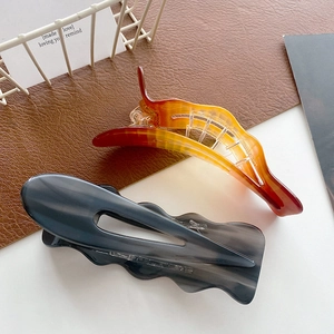 Oversized wavy acetate hair clips in amber and grey gradient on leather background