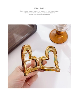 Detailed view of an amber acetate heart hair claw clip with golden metal inner teeth