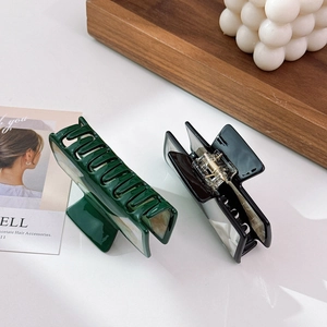 Large acetate hair claws in dark green and marbled black, shown on a rustic tray