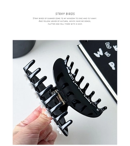 Detail of a large black acetate hair claw clip featuring white floral accents and gold spring