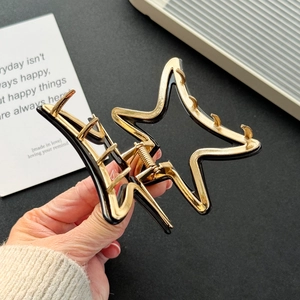 Star-shaped black and gold hair claw clip held by hand for versatile styling