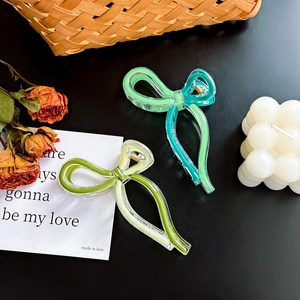 Elegant bow-shaped hair claws in two-tone resin displayed with decorative props