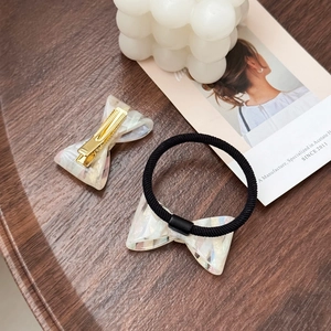 Elegant white marble acetate bow hair clip and elastic hair tie set on a wooden tray