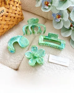 Détails de pinces à cheveux en acétate marbré vert et bleu sur texture blanche