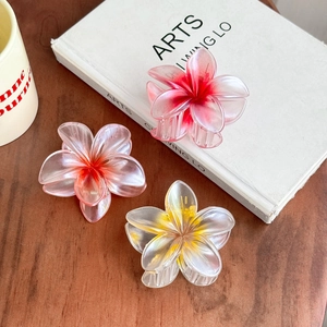 Three gradient plumeria hair claws in pink and white on a natural wooden desk