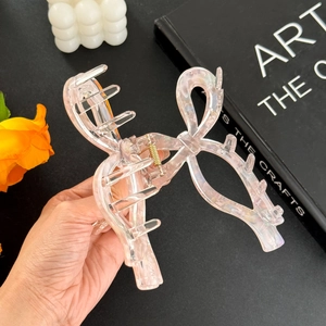 Pink iridescent acetate bow hair claw clip for thick hair shown in a hand-held view