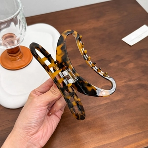 Large tortoiseshell acetate hair claw clip with vintage leopard print held by a hand