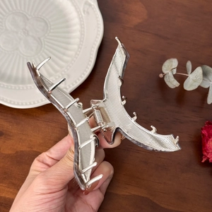 Elegant large silver metal shark hair claw clip held by hand over a wooden table